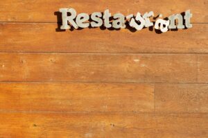 Metal letters spell "Restaurant" on a rustic wooden wall. The letters are slightly misaligned, adding a quirky charm to the scene