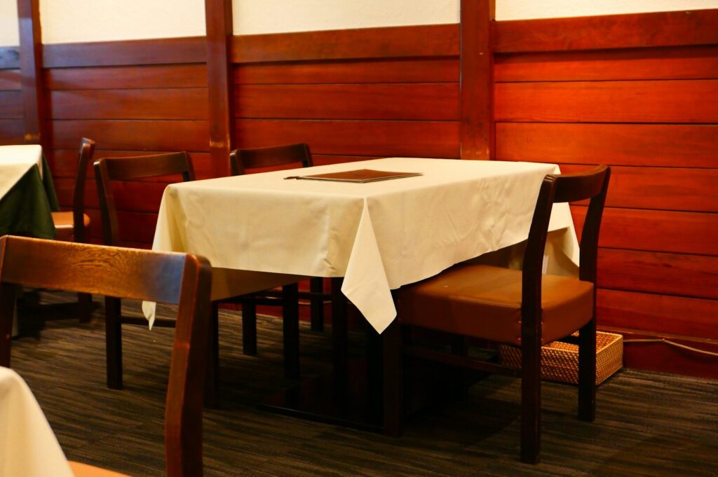 A cozy restaurant table for four with a white tablecloth and menu against warm wooden walls, creating an inviting and intimate atmosphere.