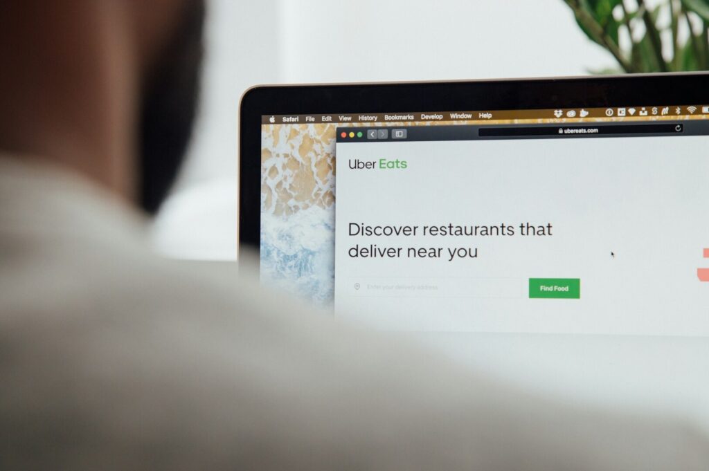 Close-up of a laptop screen displaying the Uber Eats website with the prompt "Discover restaurants that deliver near you." A blurred figure is in the foreground.