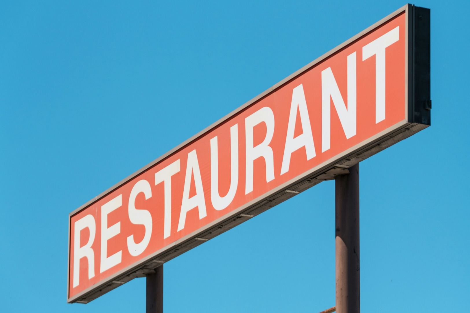A large, red rectangular sign with "RESTAURANT" in bold white letters stands against a clear blue sky, conveying a classic and inviting tone.