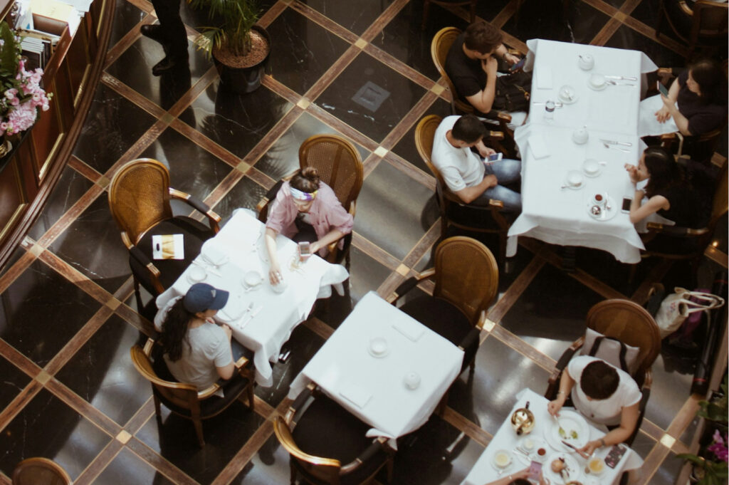 Aerial view of a bustling restaurant with elegantly set tables and patrons engaged in conversation. The polished floor and decor create a lively, refined ambiance.