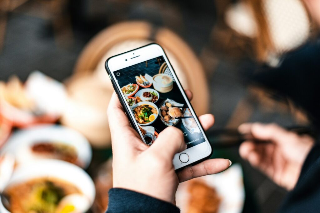 A hand holding a smartphone while capturing a photo of a beautifully plated meal, highlighting modern food photography and social sharing moments.