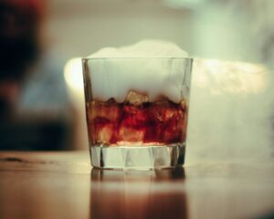 A decorative plate is held by a tattooed arm, featuring slices of baguette, a cheese wedge, and sauce, with lush green plants in a vibrant, inviting setting.