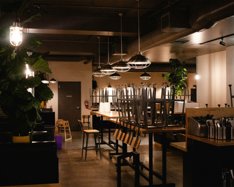 A restaurant interior with lights dimmed and chairs arranged, indicating the end of business hours for the day.