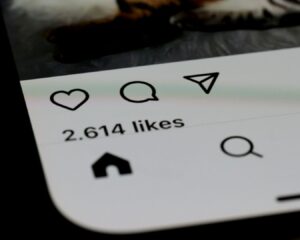 Close-up of a smartphone screen displaying a social media app interface, showing icons and "2,614 likes" text, indicating user engagement.