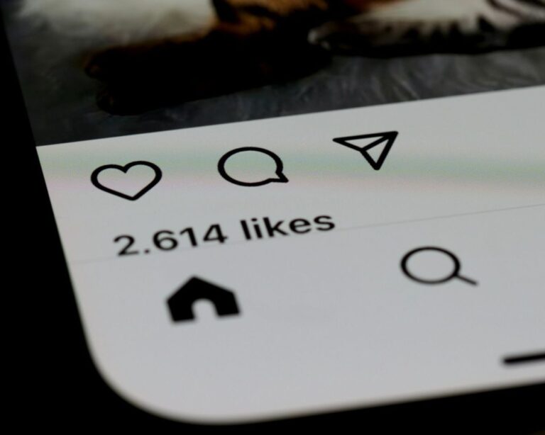 Close-up of a smartphone screen displaying a social media app interface, showing icons and "2,614 likes" text, indicating user engagement.