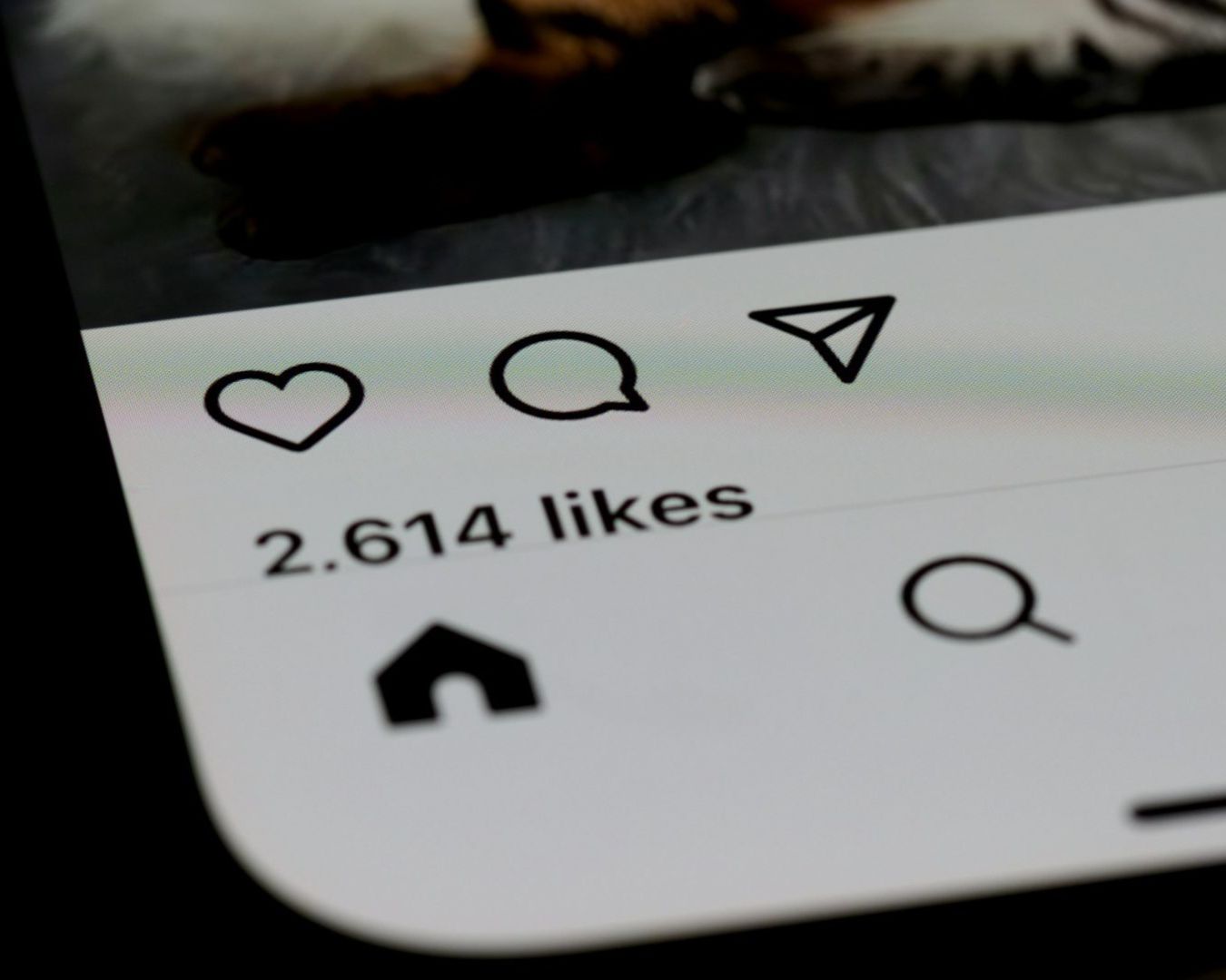 Close-up of a smartphone screen displaying a social media app interface, showing icons and "2,614 likes" text, indicating user engagement.