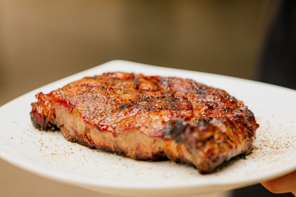 Grilled steak on a white plate, juices glistening and seasoned with pepper. The rich, browned surface conveys a feeling of savoriness and indulgence.