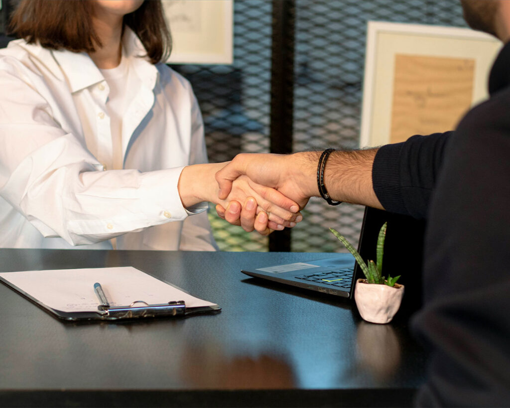 Two individuals shaking hands in a professional setting, representing partnership, agreement, or the start of a business collaboration.