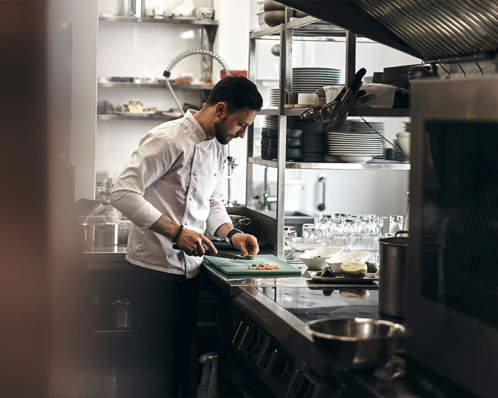 A chef carefully slicing fresh ingredients in a professional kitchen, highlighting precision, craftsmanship, and culinary focus.