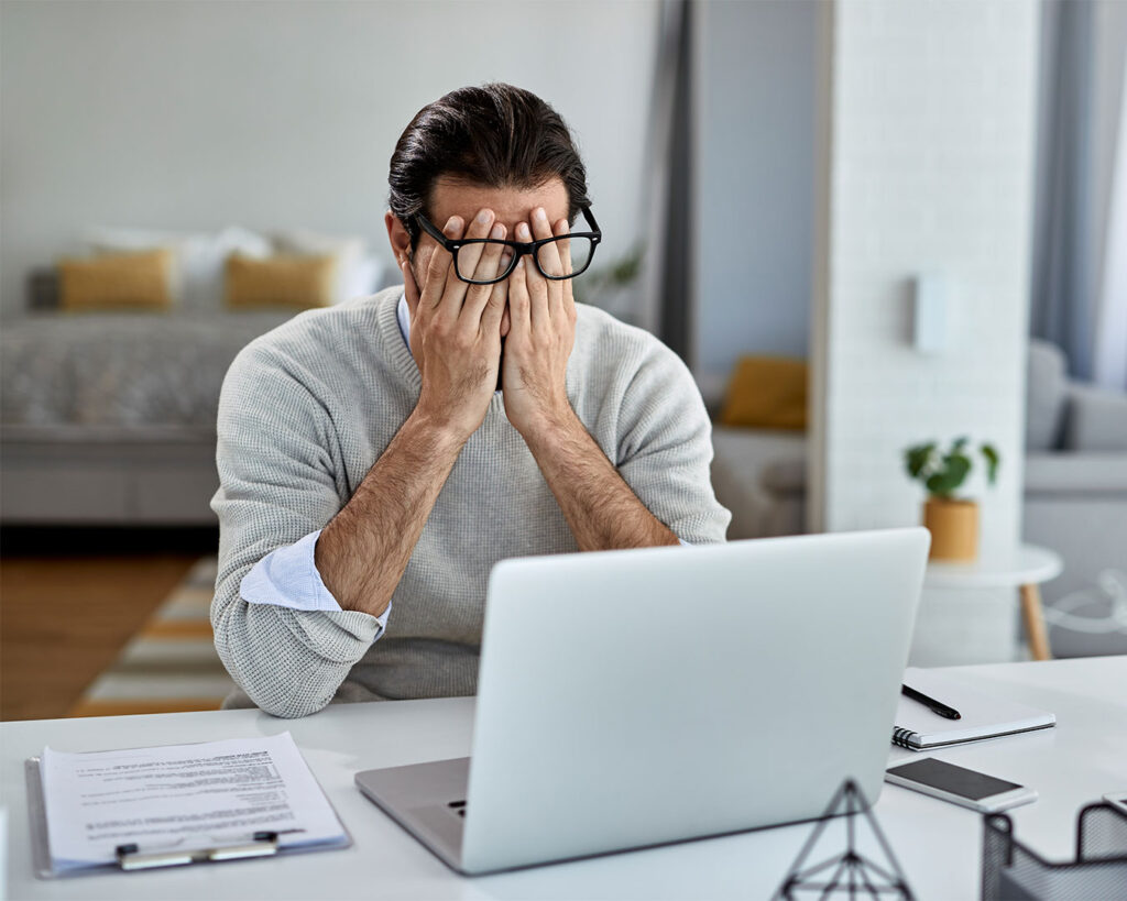 A man sitting at a work desk with his head in his hands, expressing stress and pressure from workload or business challenges.