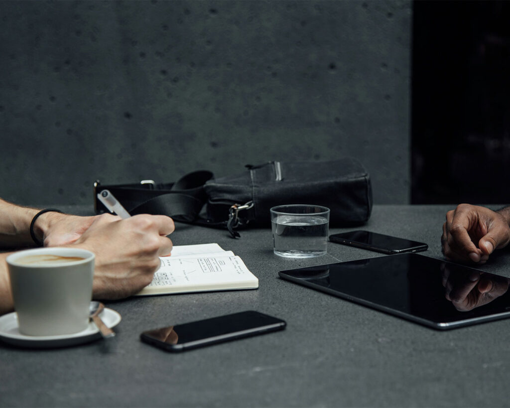 Two people sitting at a table having a discussion, using notes and gestures to plan or brainstorm ideas together.