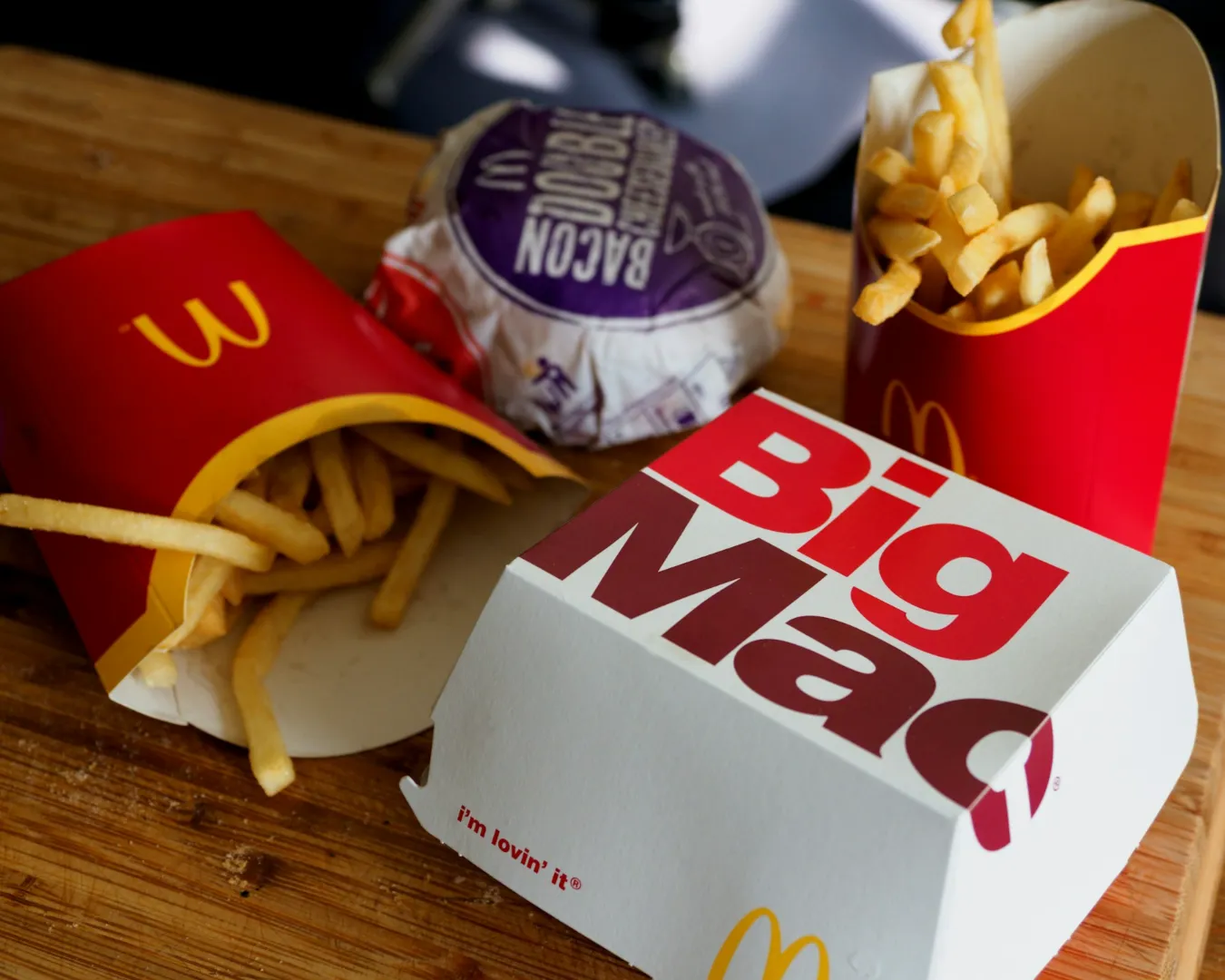 McDonald's meal with a Big Mac box, fries in red containers, and a wrapped burger on a wooden table, conveying a fast food dining experience.