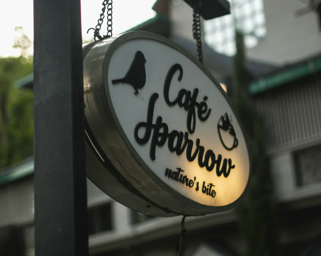 Black-and-white image of a cafe window with the text "uniek" and a steaming coffee cup logo. Reflections and cafe interior add a cozy ambiance.