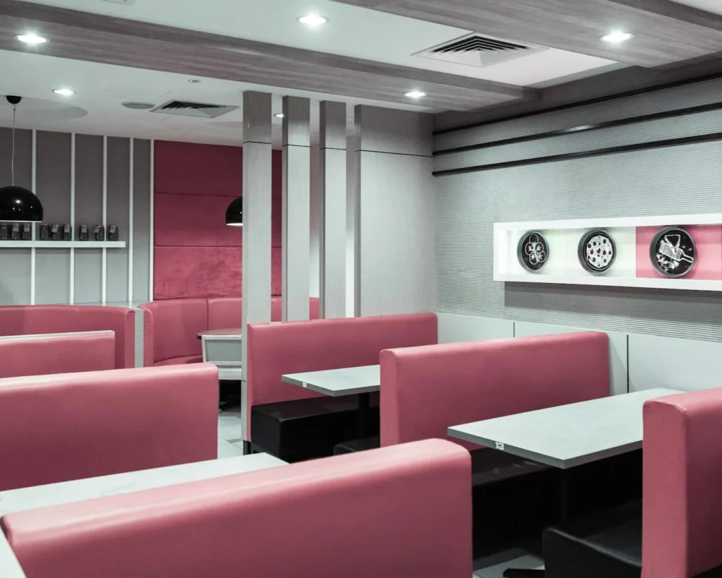 Modern diner interior with pink booths, gray tables, and wall decor featuring abstract designs. The ambiance is clean and inviting.