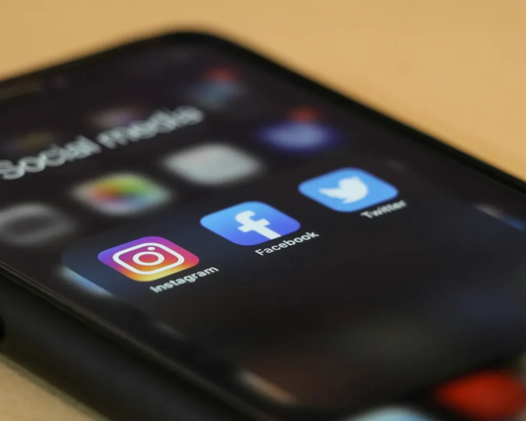 Close-up of a smartphone screen showing blurred social media icons, with Instagram, Facebook, and Twitter apps prominently displayed in focus.