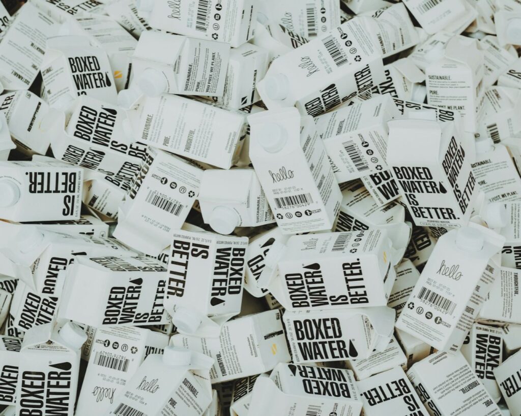 A pile of boxed water cartons, prominently displaying the text "Boxed Water is Better" and various sustainability messages.