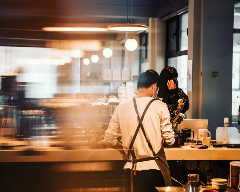 Barista with apron prepares coffee in cozy cafe, warm lighting and blurred motion create a lively and inviting atmosphere.
