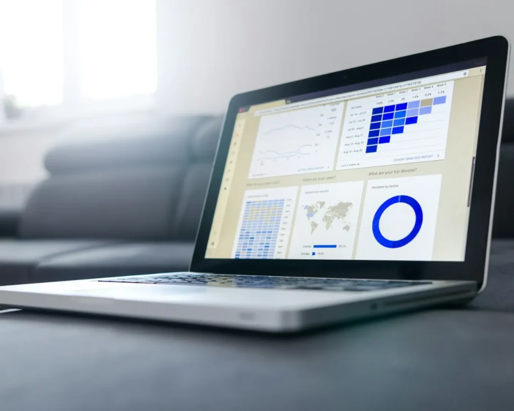 A laptop displaying data analytics charts and graphs, including line charts, a world map, and pie charts, set on a sofa, conveying a work-from-home vibe.