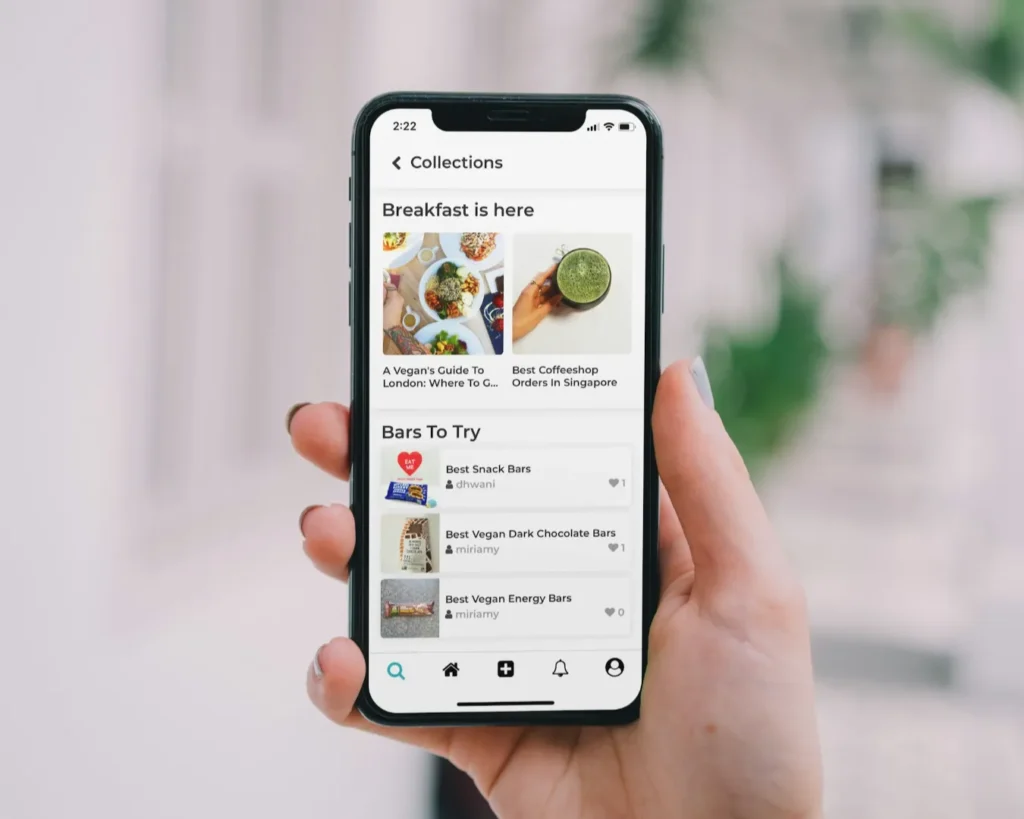 A hand holds a smartphone displaying a food app. Sections labeled "Breakfast is here" and "Bars To Try" show images of meals and snacks, suggesting a modern, healthy lifestyle.