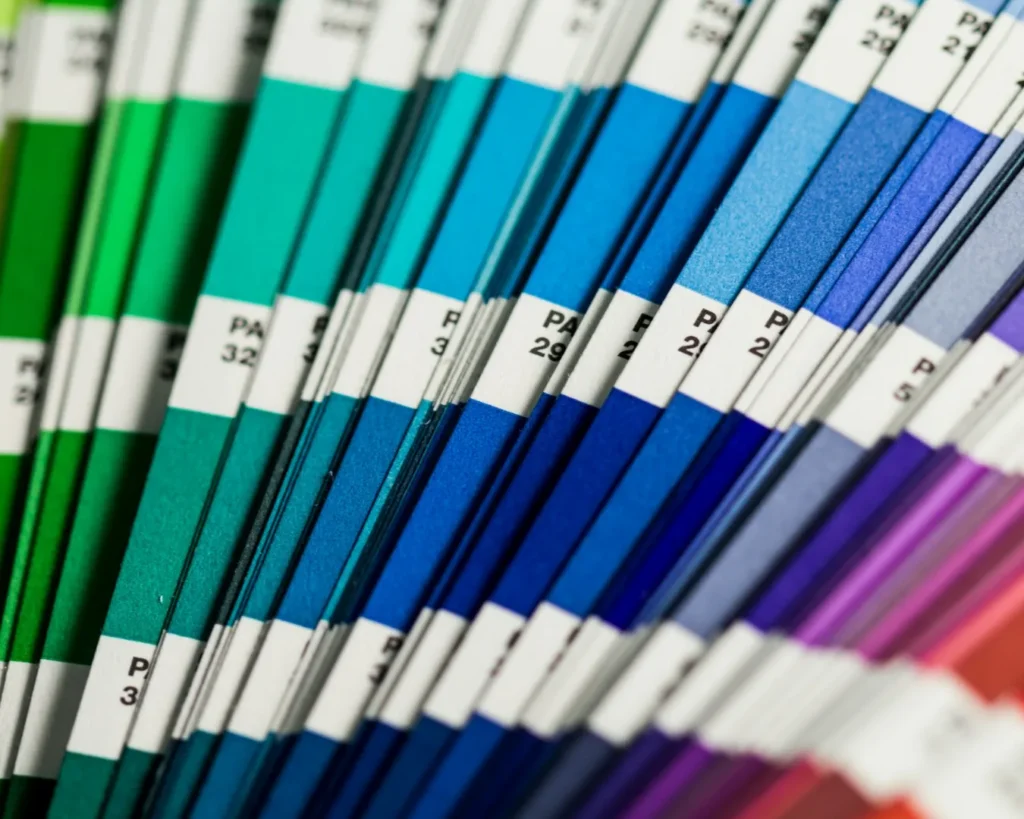 A close-up of a color fan deck featuring an array of vibrant swatches. The shades transition smoothly from green to blue to purple, creating a vivid gradient.