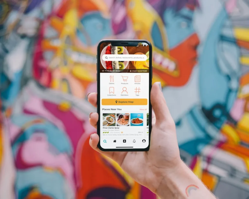 A hand holds a smartphone displaying a food app interface against a colorful graffiti wall. Vibrant tones highlight an urban, modern vibe.