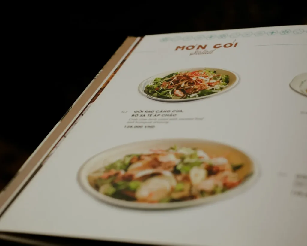 A close-up of a menu page titled "Salad" features two dishes with colorful photos. The page has elegant design elements and pricing details.