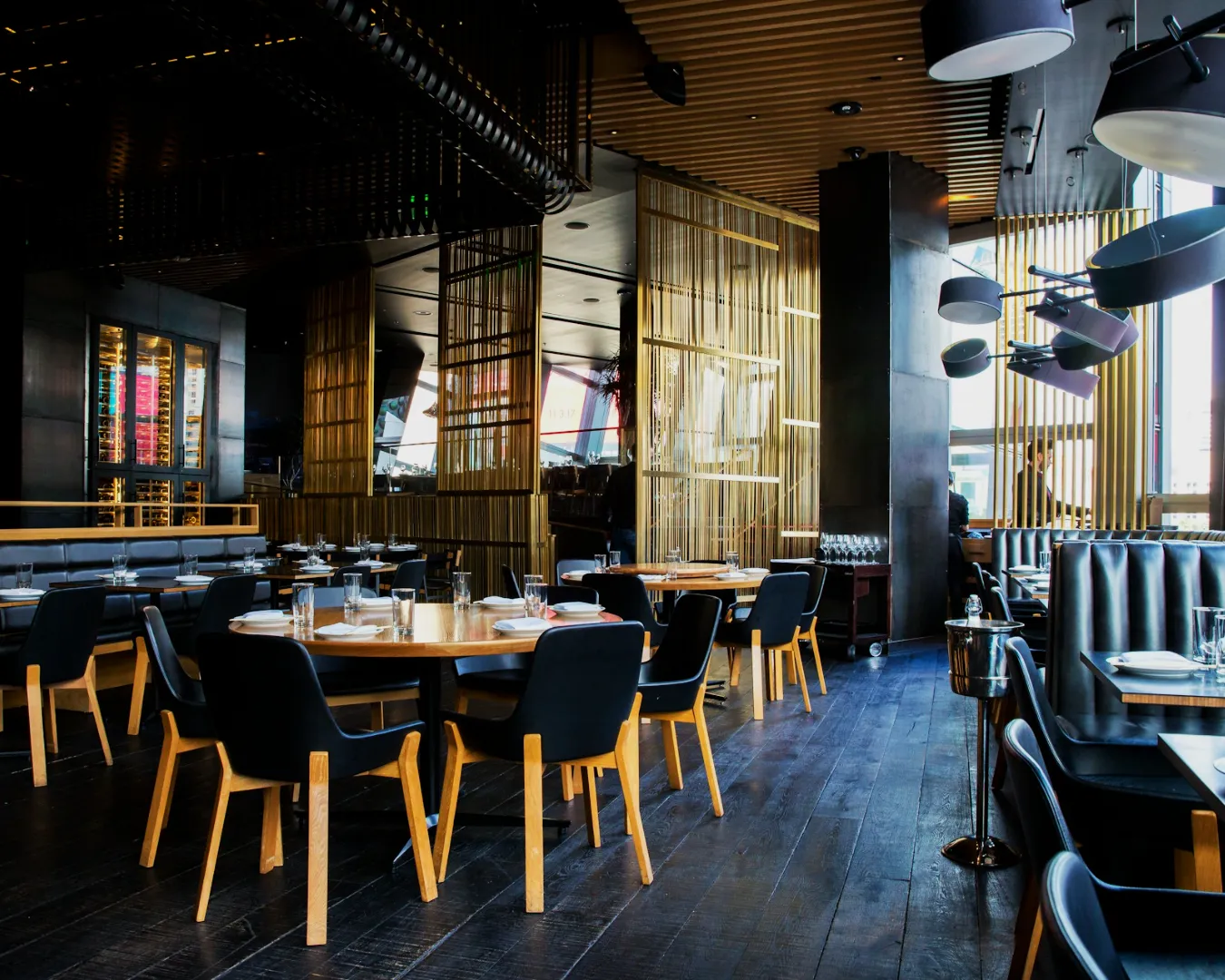 Modern restaurant interior with sleek black chairs and wooden tables, elegant lighting fixtures, and floor-to-ceiling windows, creating a stylish ambiance.