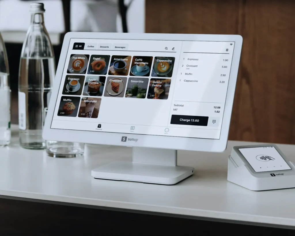 A modern point-of-sale system on a counter beside water bottles. The screen displays a menu with coffee and pastry options. The setting is sleek and efficient.