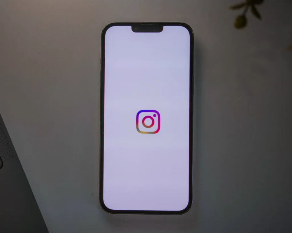 Smartphone on a table displaying the Instagram logo on a bright white screen, suggesting connectivity and social media engagement.
