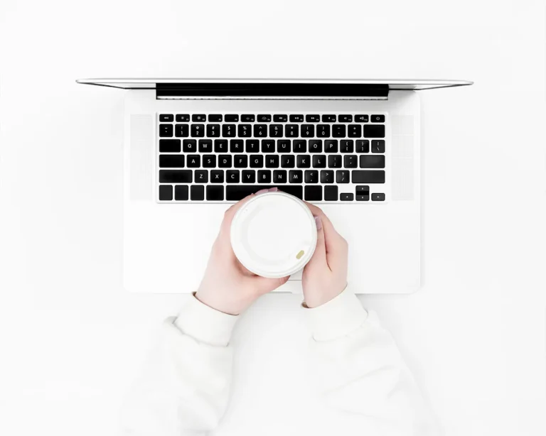 Minimal overhead shot of a laptop with a coffee cup on a clean white desk, representing restaurant website branding and digital customer experience strategy
