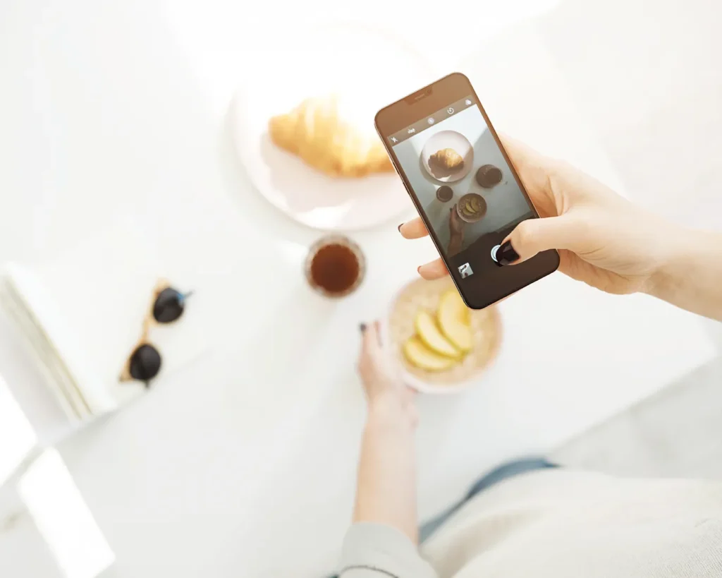 Hand holding smartphone photographing café brunch for restaurant digital marketing and social media branding