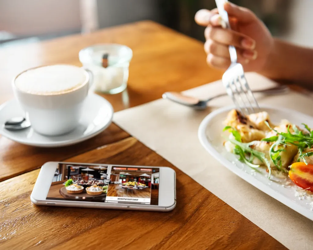 Customer browsing a restaurant website on a smartphone beside plated café food, highlighting mobile-friendly restaurant branding and online menu design