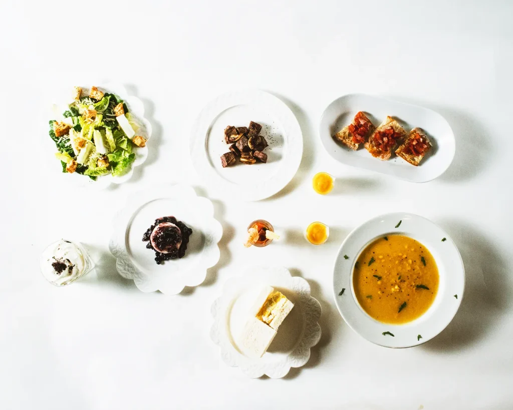 Overhead flat lay of assorted restaurant dishes on white table, illustrating menu overcrowding and concept erosion in Singapore F&B operations