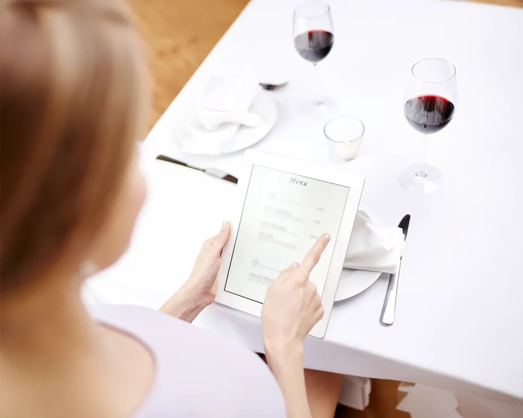Customer browsing a digital tablet restaurant menu in an upscale dining environment, representing modern menu design and seamless guest experience