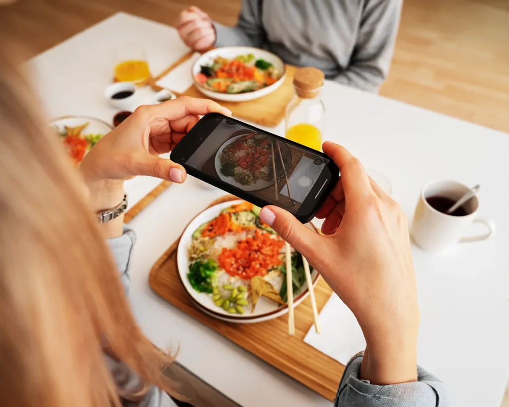 Diner taking food photo with smartphone in restaurant, illustrating user-generated content and social media marketing for Singapore F&B brands