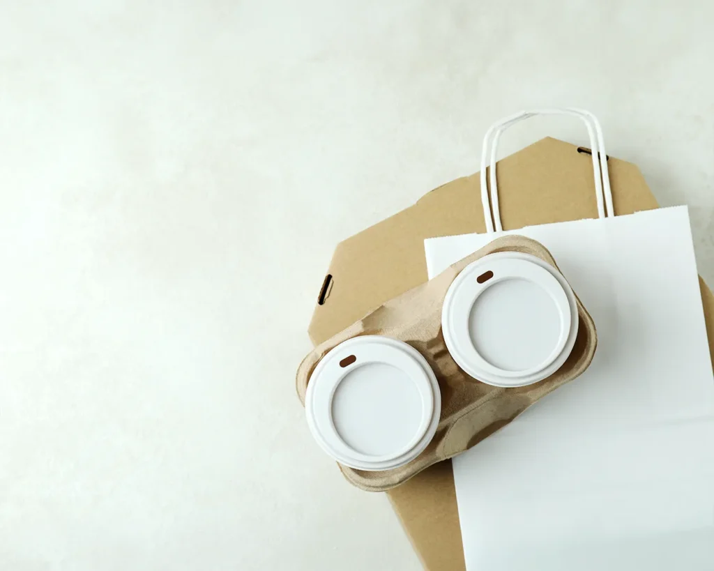 Minimal branded takeaway coffee cups and packaging on a neutral background, symbolizing cohesive restaurant brand identity across digital and physical touchpoints