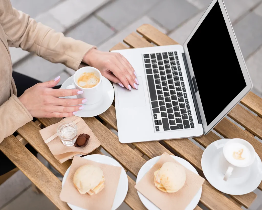 Woman using laptop with coffee and café breakfast outdoors representing consistent restaurant digital branding and customer experience after rebrand