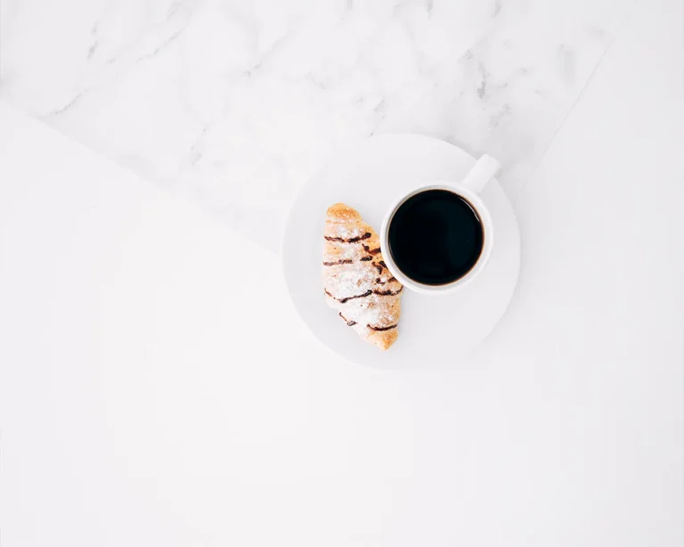 Minimalist coffee and pastry flat lay on white marble table, restaurant brand voice planning and hospitality marketing concept