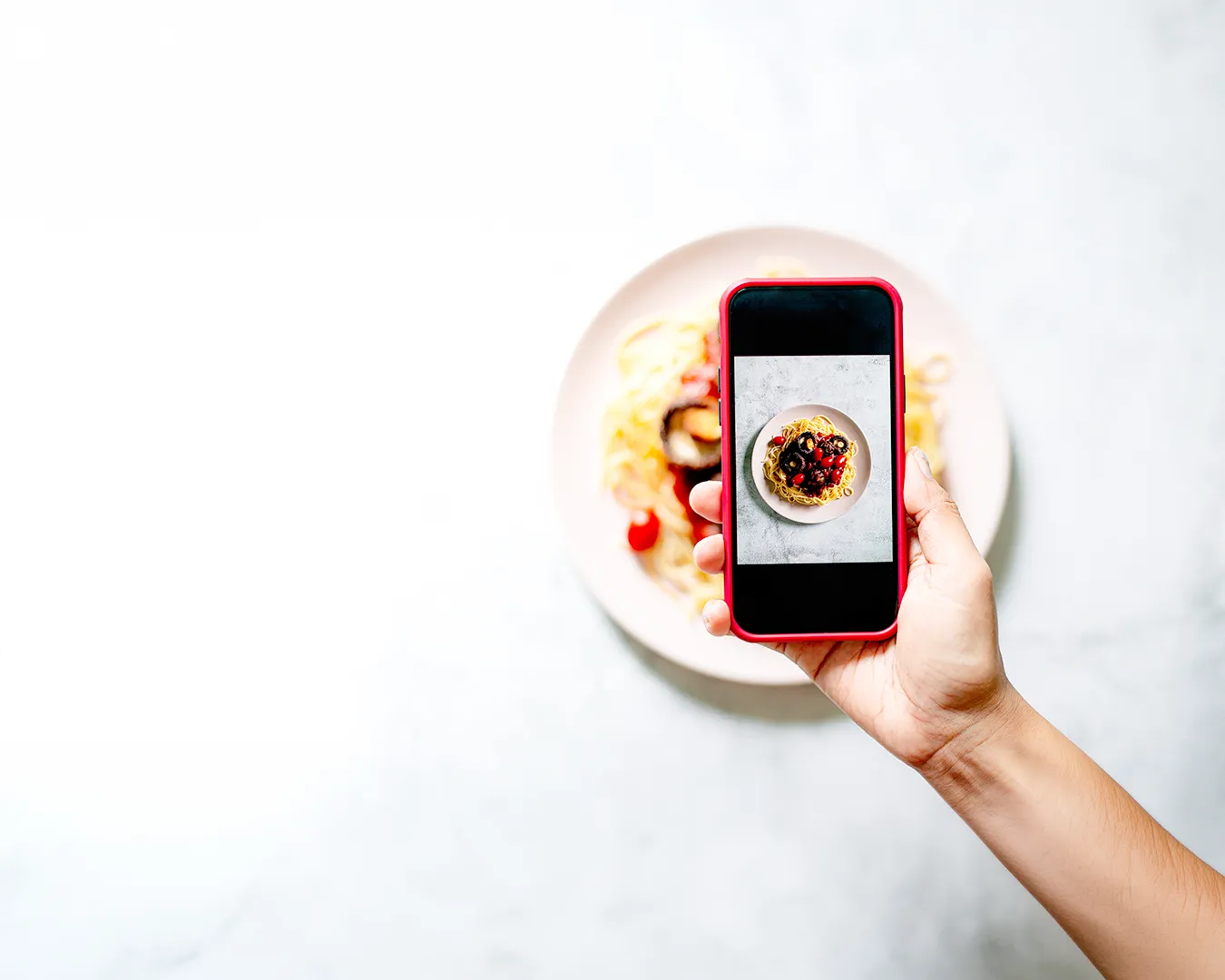 Hand holding smartphone photographing a plated pasta dish for restaurant social media content