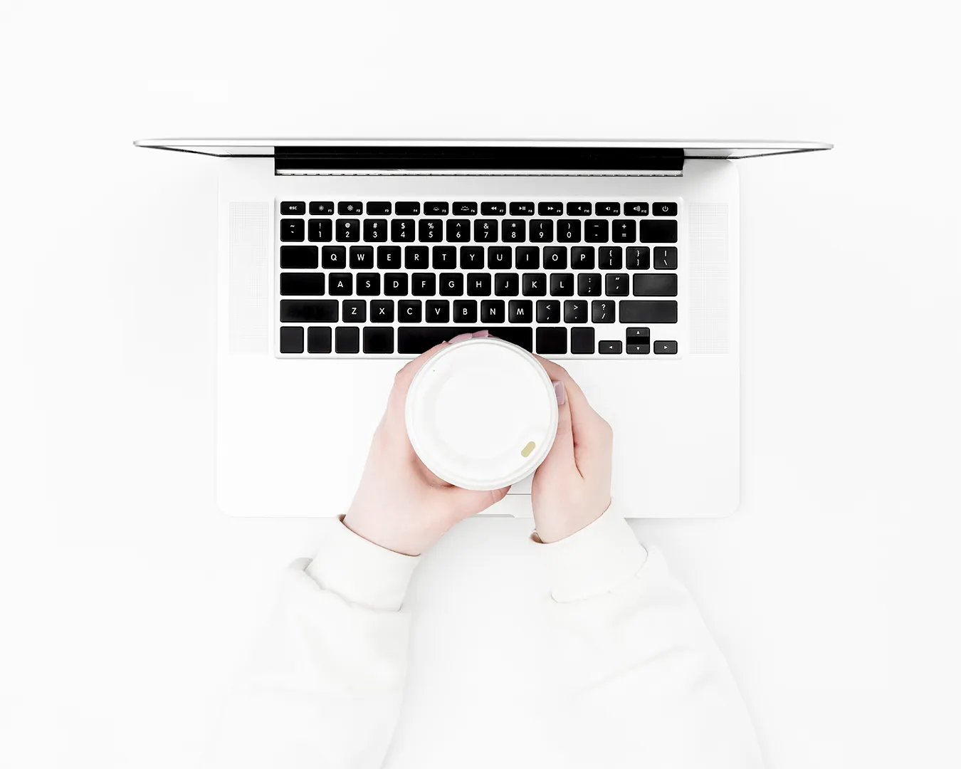 Person holding coffee cup over laptop on minimalist white workspace
