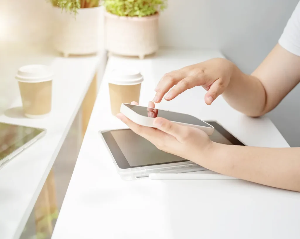 Restaurant owner reviewing social media content on smartphone beside tablet and coffee while managing restaurant digital marketing and online brand consistency.