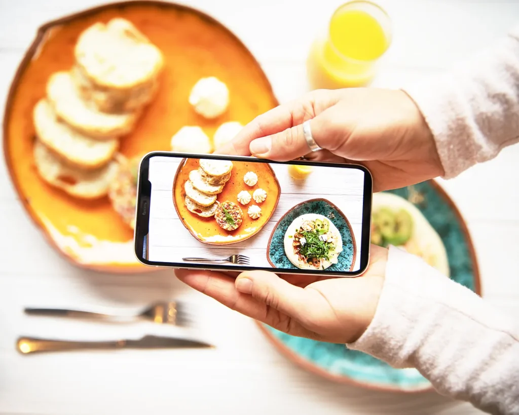 Customer using smartphone to capture food photography of colorful restaurant dishes for online marketing