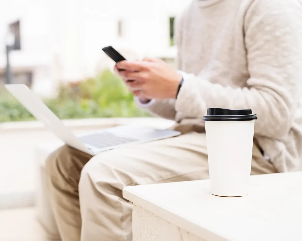 Restaurant manager using smartphone and laptop to monitor Instagram marketing, website updates, and digital customer engagement in a café setting.
