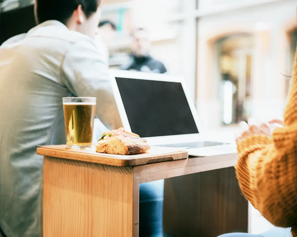 Restaurant guests using a laptop at a café table with food and drinks during a casual meeting