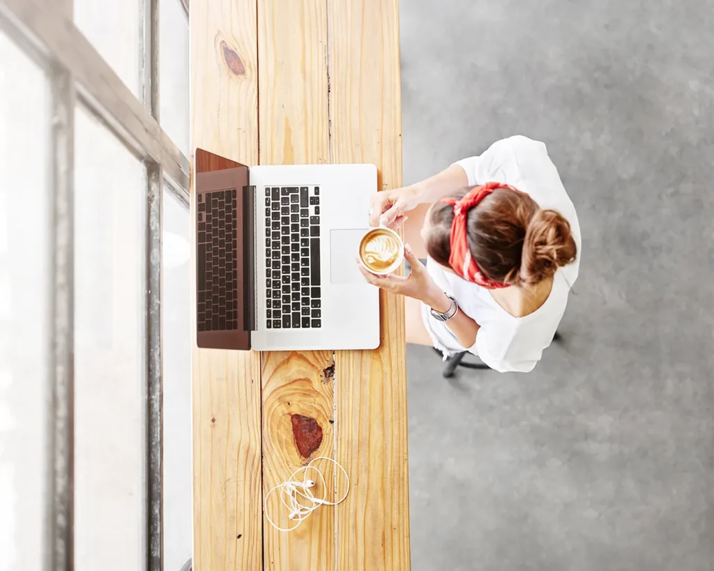 Overhead view of person using laptop with coffee at wooden café table