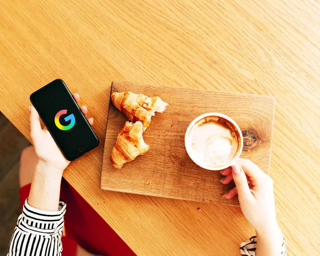 Customer searching Google on smartphone at cafe table, restaurant discovery online, local search marketing, Google Business Profile visibility for restaurants