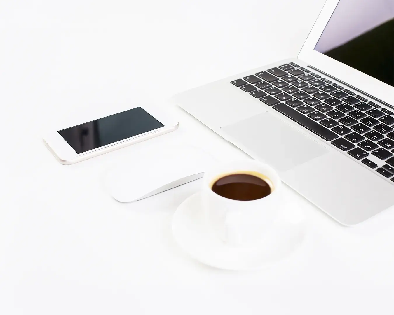 Restaurant digital marketing budget planning workspace with laptop, smartphone, and coffee on a minimalist white desk