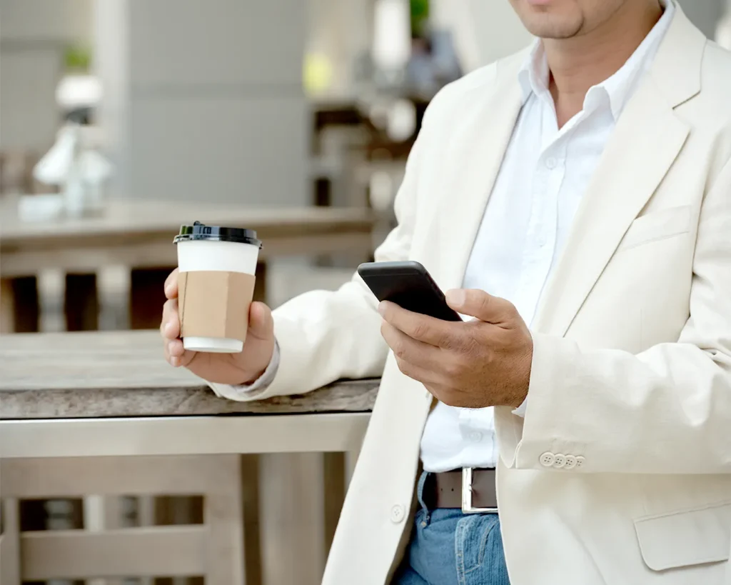 Restaurant owner checking smartphone with takeaway coffee while managing promotional campaigns and customer communication.