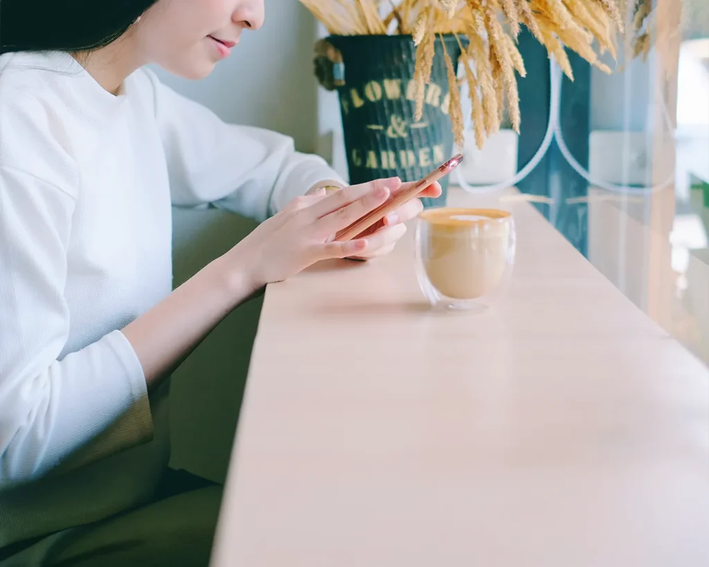 Customer using smartphone at a modern café, representing web-based restaurant rewards, digital loyalty program, and mobile engagement.